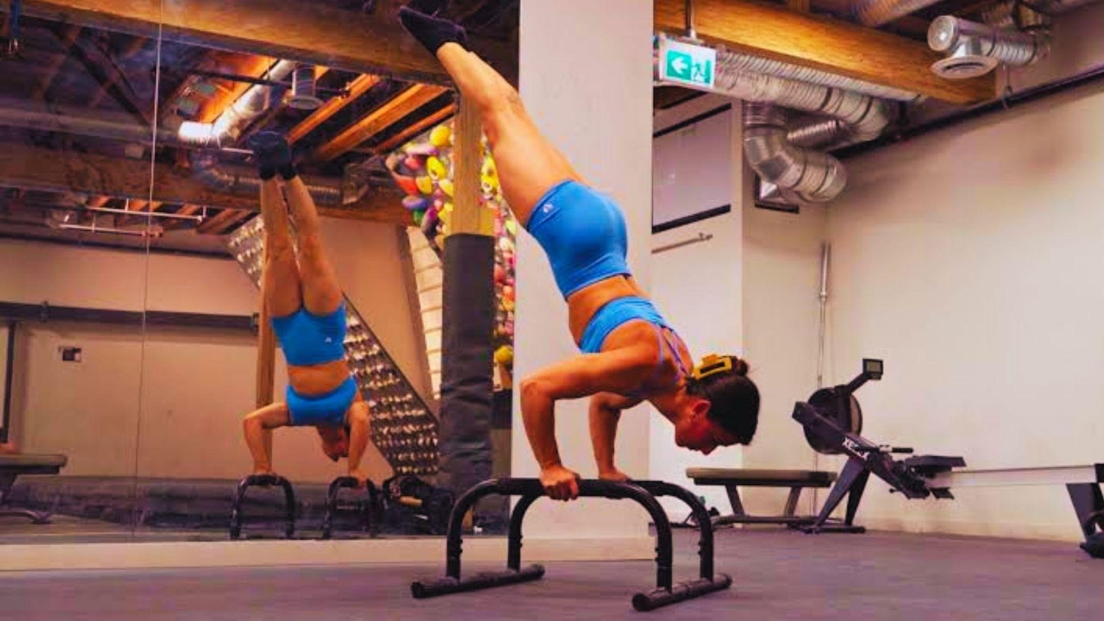A woman executing a handstand on a bar, demonstrating athleticism and control in a fitness environment.