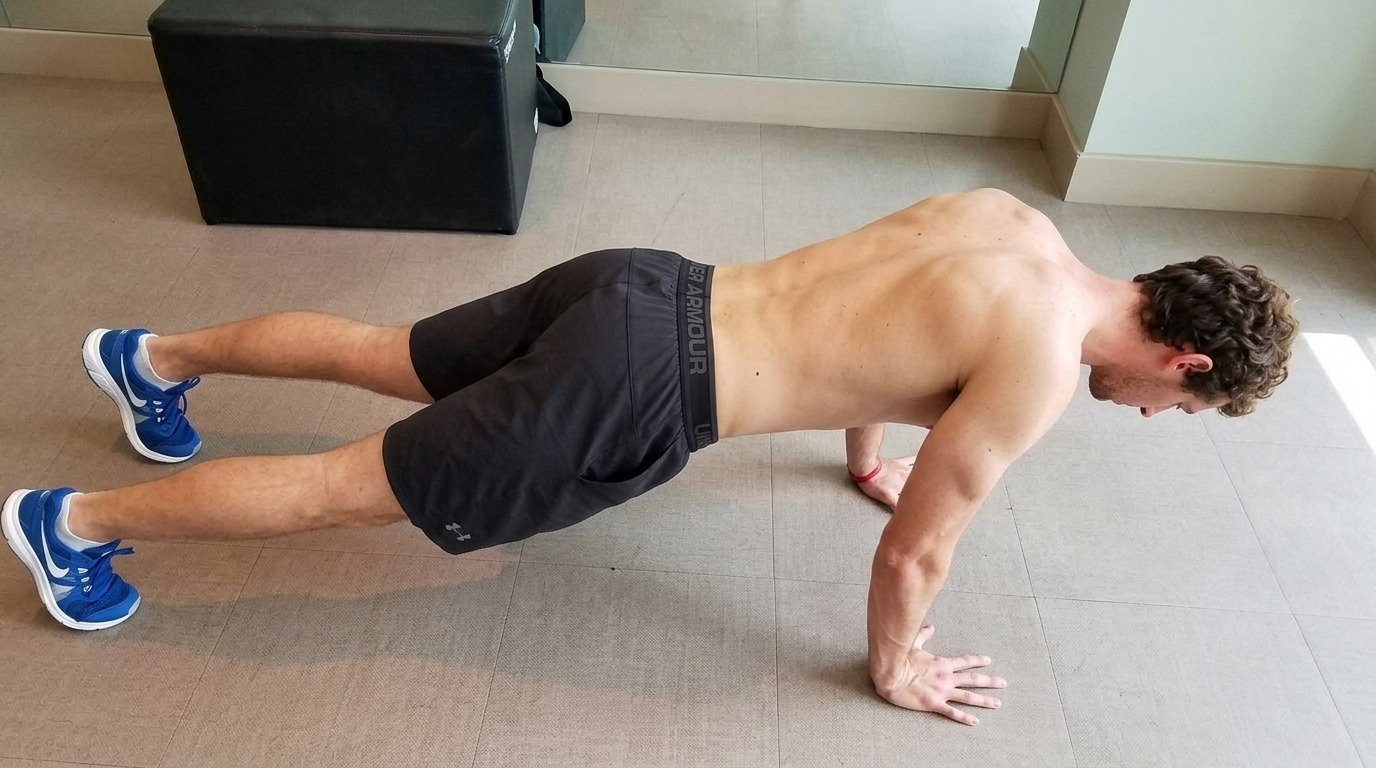Man doing the push-up with a plus, his shoulder blades spreading and his upper back rounding.
