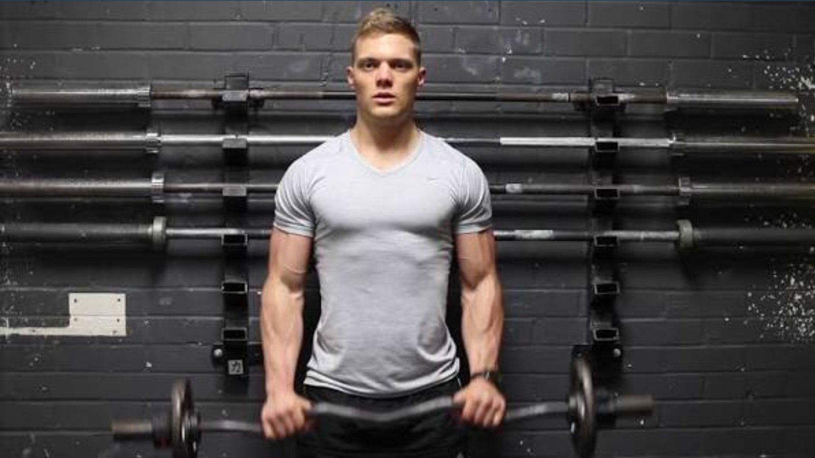 Man performs reverse grip EZ bar curl inside the gym.