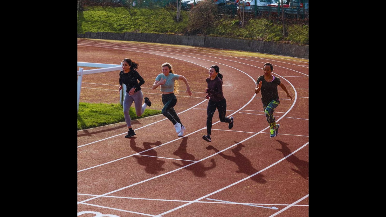 Four diverse female athletes sprinting competitively on an outdoor running track.