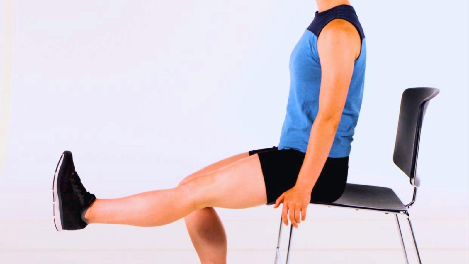 Women in blue tank top extends legs on leg extension machine in dark gym, grimacing, weight stack visible behind.