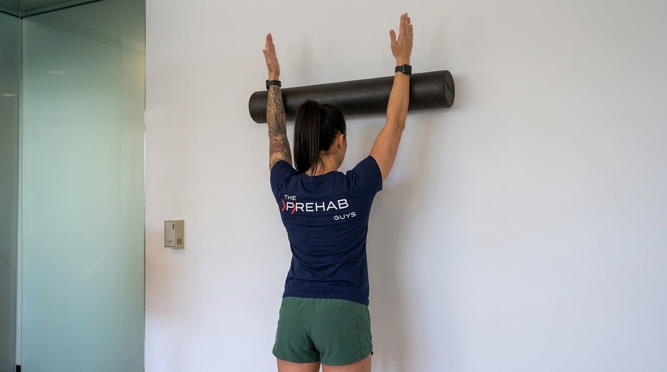 Woman doing the wall slide with a foam roll, facing the wall.