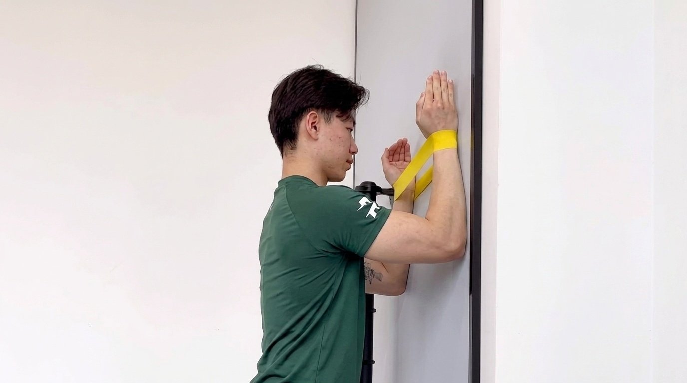 Man doing the serratus wall walks with a resistance band wrapped around his wrists.