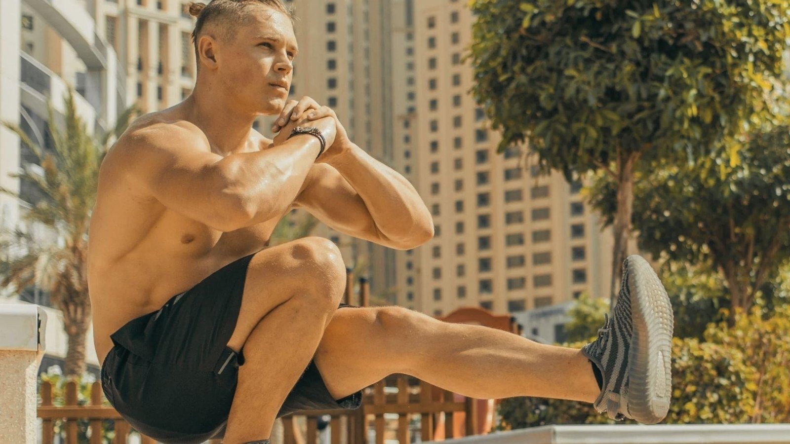 A shirtless man performs squats on a city street, showcasing his fitness routine against an urban backdrop.