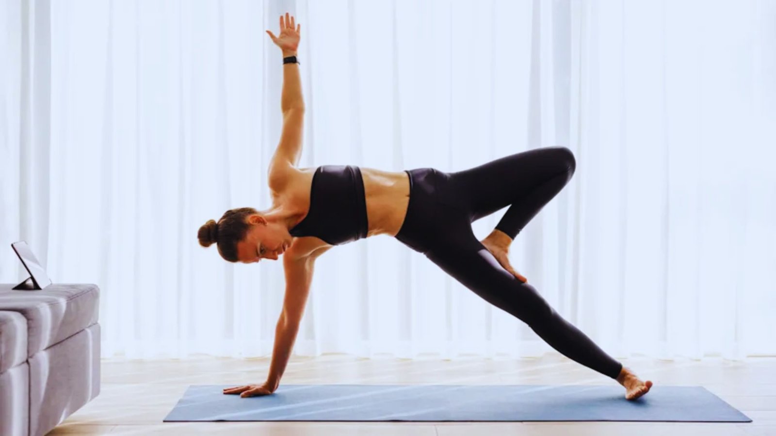 A woman smiles while holding a side plank pose on a gym mat during a Pilates session.