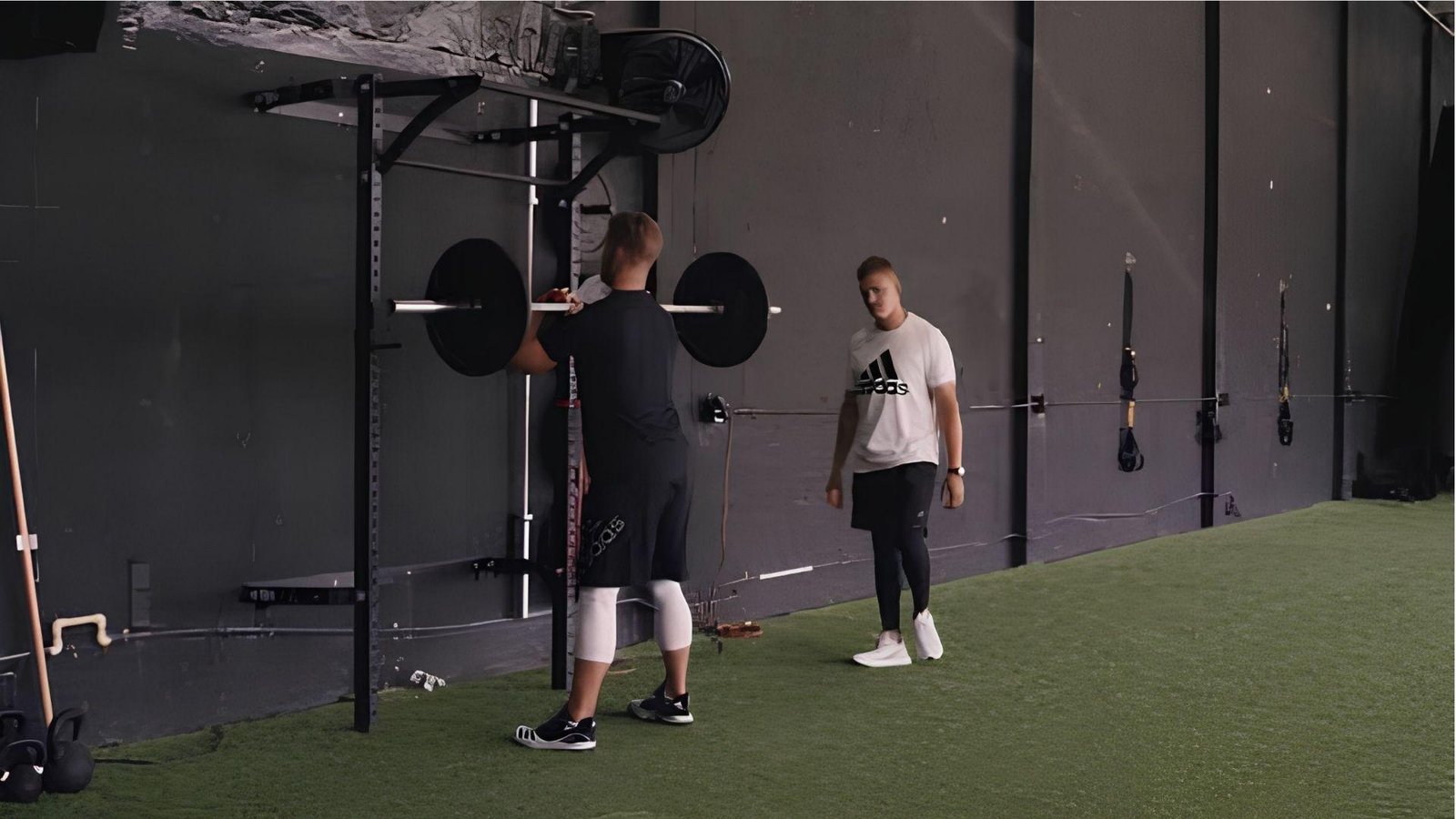 Baseball player doing front squats with barbell while coach spots