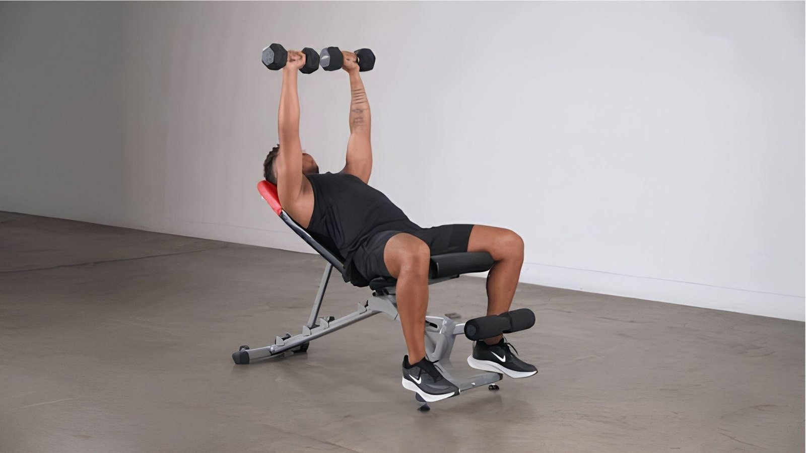 Man doing incline dumbbell bench press on adjustable bench in empty gym studio.