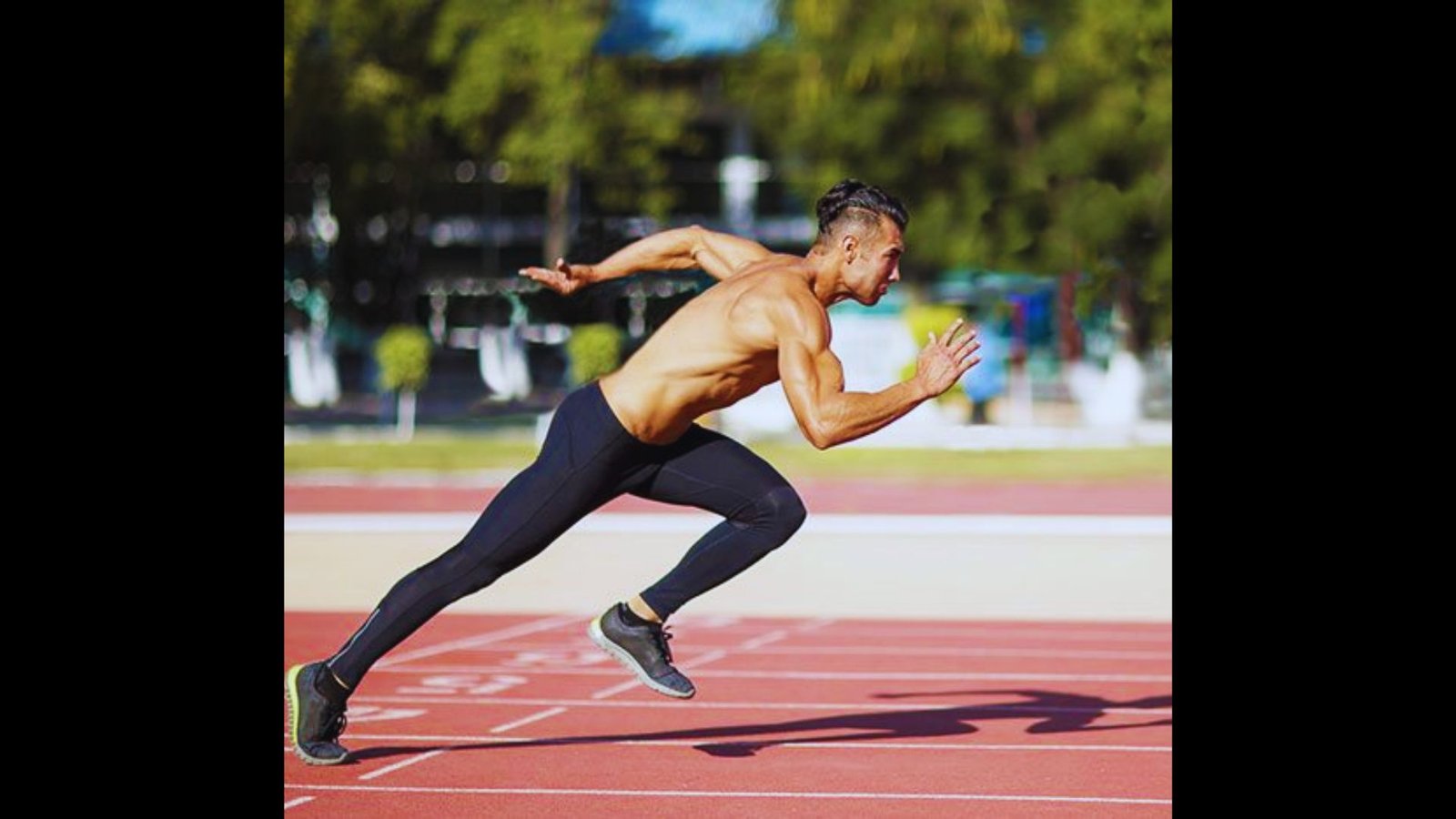 Male sprinter in mid-stride during a workout on an outdoor track.