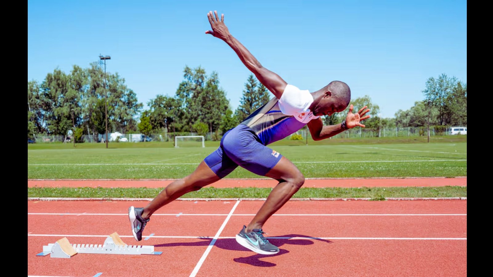 A male track athlete sprinting mid-stride on an outdoor running track.