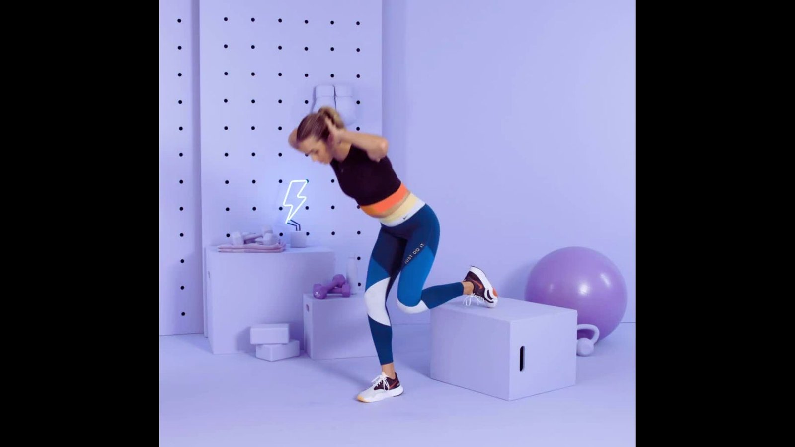 An athletic woman mid-leap, performing a box jump onto a white platform in a brightly lit studio.