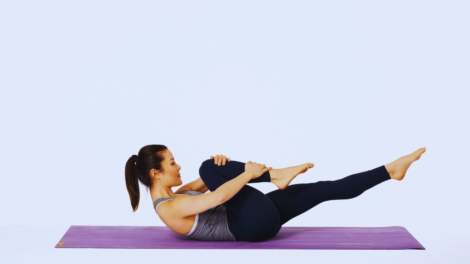 A woman doing a Mat Pilates crunch exercise on a purple mat.