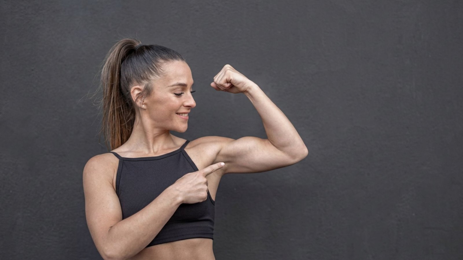 Woman flexing her bicep and pointing at her arm muscle while smiling.