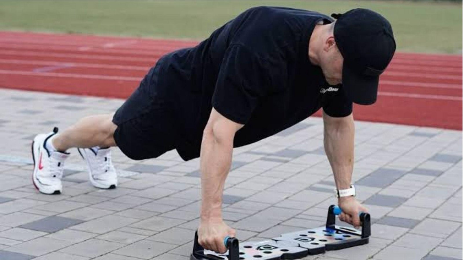 Man in black outfit doing push-ups on push up board at outdoor track
