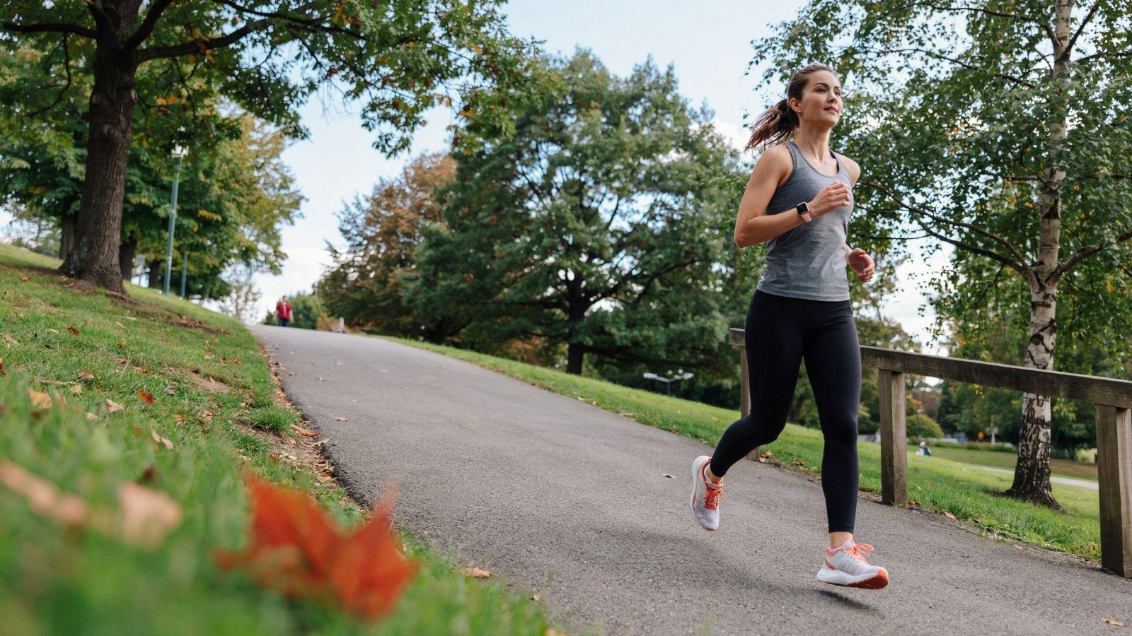 An athletic woman smiling while jogging on an outdoor path on a sunny day.