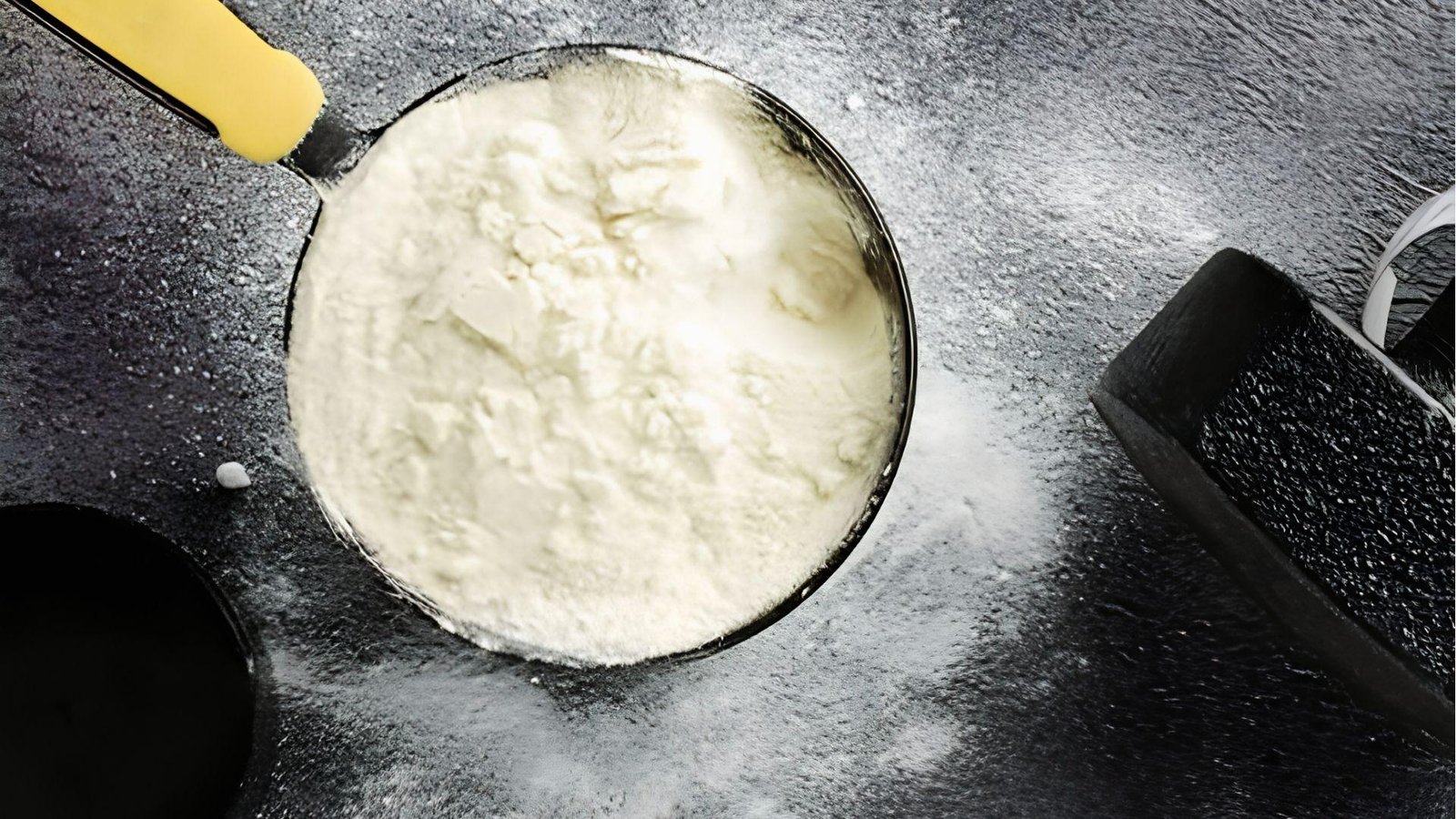 Top view of white pre workout powder in scoop with yellow handle on dark surface