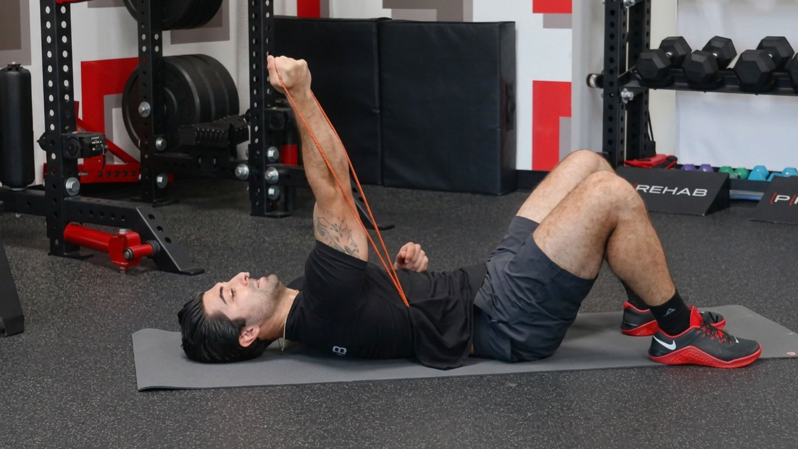 Man lying on a mat doing a resistance band tricep extension exercise.
